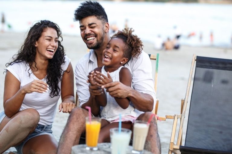 happy family of three laughing on beach with drinks